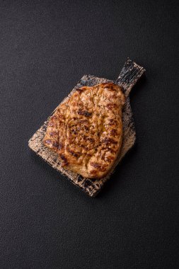 Koyu beton bir arka planda ızgara biftek veya tuzlu, baharatlı ve otlu domuz eti.