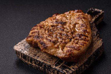 Koyu beton bir arka planda ızgara biftek veya tuzlu, baharatlı ve otlu domuz eti.