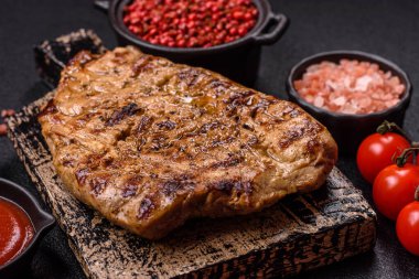 Koyu beton bir arka planda ızgara biftek veya tuzlu, baharatlı ve otlu domuz eti.