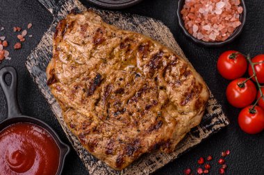 Koyu beton bir arka planda ızgara biftek veya tuzlu, baharatlı ve otlu domuz eti.