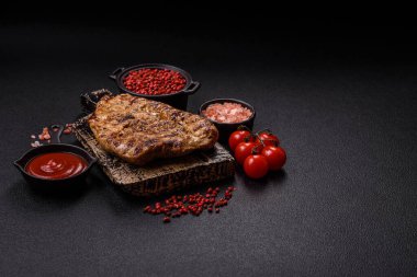 Koyu beton bir arka planda ızgara biftek veya tuzlu, baharatlı ve otlu domuz eti.