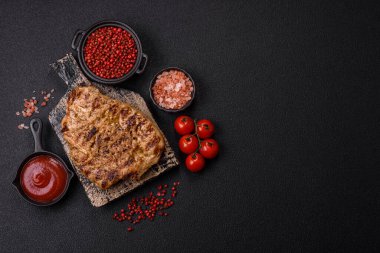 Koyu beton bir arka planda ızgara biftek veya tuzlu, baharatlı ve otlu domuz eti.