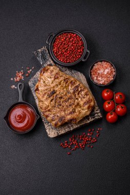 Koyu beton bir arka planda ızgara biftek veya tuzlu, baharatlı ve otlu domuz eti.