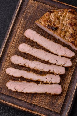 Koyu beton bir arka planda ızgara biftek veya tuzlu, baharatlı ve otlu domuz eti.