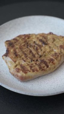 Koyu beton bir arka planda ızgara biftek veya tuzlu, baharatlı ve otlu domuz eti.