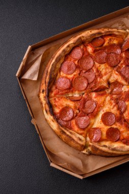 Sosisli biberli pizza, mozzarella peyniri, domates, tuz ve baharatlar koyu beton arka planda.