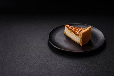 Lezzetli taze cheesecake keki ya da koyu beton arka planda seramik tabakta kremalı ve fındıklı snickers.