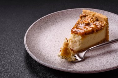 Lezzetli taze cheesecake keki ya da koyu beton arka planda seramik tabakta kremalı ve fındıklı snickers.