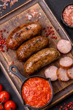 Tuzlu, baharatlı ve otlu sulu sosisler koyu beton arka planda kızartılıyor.