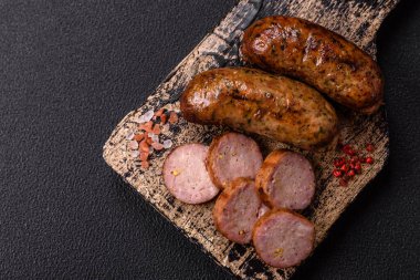 Tuzlu, baharatlı ve otlu sulu sosisler koyu beton arka planda kızartılıyor.