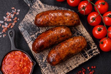 Tuzlu, baharatlı ve otlu sulu sosisler koyu beton arka planda kızartılıyor.