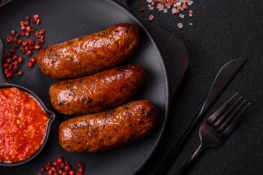Tuzlu, baharatlı ve otlu sulu sosisler koyu beton arka planda kızartılıyor.