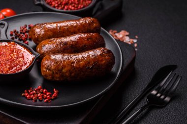 Tuzlu, baharatlı ve otlu sulu sosisler koyu beton arka planda kızartılıyor.