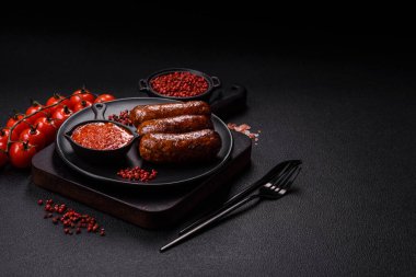 Tuzlu, baharatlı ve otlu sulu sosisler koyu beton arka planda kızartılıyor.