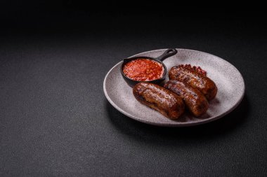 Tuzlu, baharatlı ve otlu sulu sosisler koyu beton arka planda kızartılıyor.