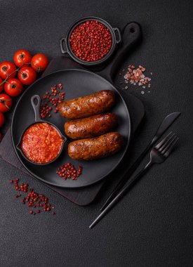 Tuzlu, baharatlı ve otlu sulu sosisler koyu beton arka planda kızartılıyor.