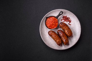 Tuzlu, baharatlı ve otlu sulu sosisler koyu beton arka planda kızartılıyor.