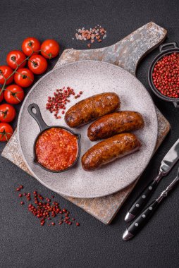 Tuzlu, baharatlı ve otlu sulu sosisler koyu beton arka planda kızartılıyor.