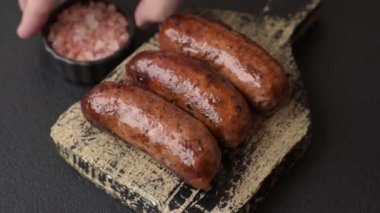 Tuzlu, baharatlı ve otlu sulu sosisler koyu beton arka planda kızartılıyor.