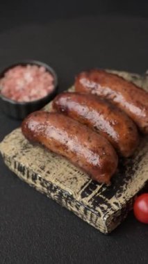 Tuzlu, baharatlı ve otlu sulu sosisler koyu beton arka planda kızartılıyor.