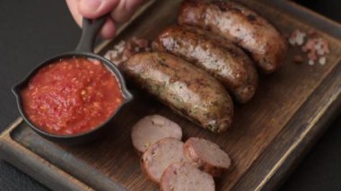 Tuzlu, baharatlı ve otlu sulu sosisler koyu beton arka planda kızartılıyor.