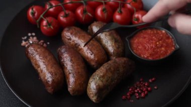 Tuzlu, baharatlı ve otlu sulu sosisler koyu beton arka planda kızartılıyor.