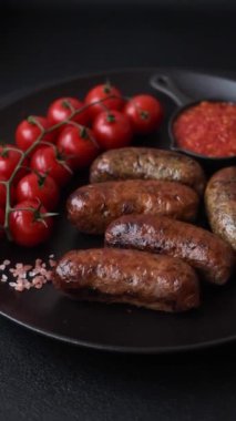 Tuzlu, baharatlı ve otlu sulu sosisler koyu beton arka planda kızartılıyor.