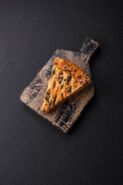 Pieces of quiche with salmon, spinach or broccoli, salt and spices on a dark concrete background