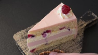 Bir parça tatlı kek pembe kremalı ahududu aromalı, kurabiyeli, peynirli kek koyu betondan arka planda.