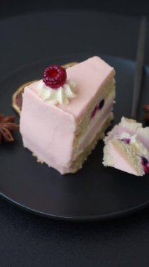 Bir parça tatlı kek pembe kremalı ahududu aromalı, kurabiyeli, peynirli kek koyu betondan arka planda.