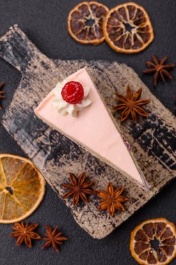 Bir parça tatlı kek pembe kremalı ahududu aromalı, kurabiyeli, peynirli kek koyu betondan arka planda.