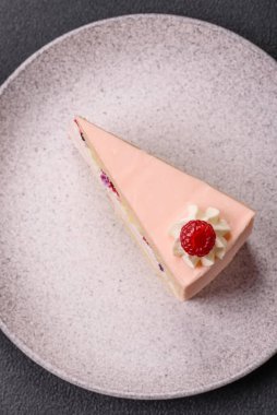 Bir parça tatlı kek pembe kremalı ahududu aromalı, kurabiyeli, peynirli kek koyu betondan arka planda.