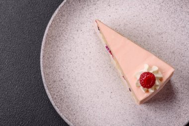 Bir parça tatlı kek pembe kremalı ahududu aromalı, kurabiyeli, peynirli kek koyu betondan arka planda.