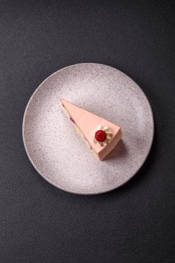 Bir parça tatlı kek pembe kremalı ahududu aromalı, kurabiyeli, peynirli kek koyu betondan arka planda.