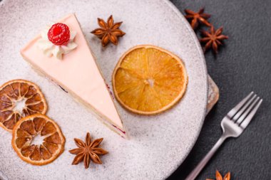 Bir parça tatlı kek pembe kremalı ahududu aromalı, kurabiyeli, peynirli kek koyu betondan arka planda.