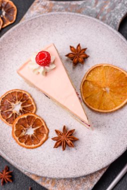 Bir parça tatlı kek pembe kremalı ahududu aromalı, kurabiyeli, peynirli kek koyu betondan arka planda.