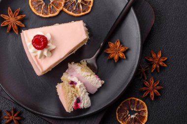 Bir parça tatlı kek pembe kremalı ahududu aromalı, kurabiyeli, peynirli kek koyu betondan arka planda.