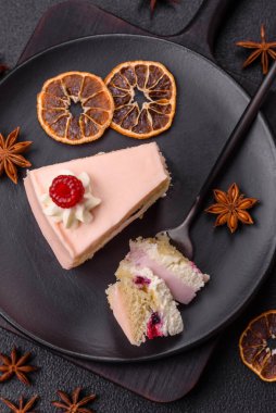 Bir parça tatlı kek pembe kremalı ahududu aromalı, kurabiyeli, peynirli kek koyu betondan arka planda.