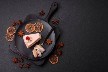 Bir parça tatlı kek pembe kremalı ahududu aromalı, kurabiyeli, peynirli kek koyu betondan arka planda.