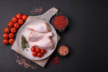 Raw chicken legs with salt, spices, herbs and tomatoes on a dark concrete background clipart