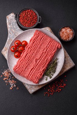 Tuzlu, baharatlı, otlu ve domatesli, koyu beton arkaplanlı çiğ et veya domuz eti.