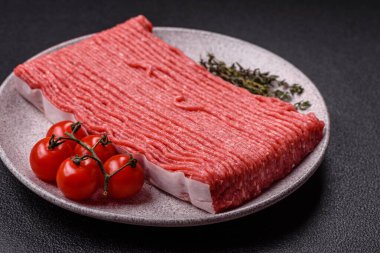 Tuzlu, baharatlı, otlu ve domatesli, koyu beton arkaplanlı çiğ et veya domuz eti.