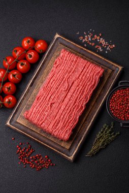 Tuzlu, baharatlı, otlu ve domatesli, koyu beton arkaplanlı çiğ et veya domuz eti.