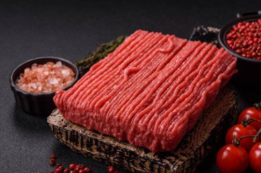 Tuzlu, baharatlı, otlu ve domatesli, koyu beton arkaplanlı çiğ et veya domuz eti.