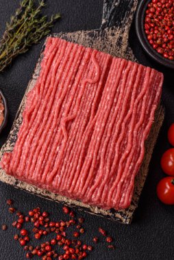 Tuzlu, baharatlı, otlu ve domatesli, koyu beton arkaplanlı çiğ et veya domuz eti.