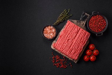 Tuzlu, baharatlı, otlu ve domatesli, koyu beton arkaplanlı çiğ et veya domuz eti.