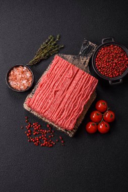 Tuzlu, baharatlı, otlu ve domatesli, koyu beton arkaplanlı çiğ et veya domuz eti.