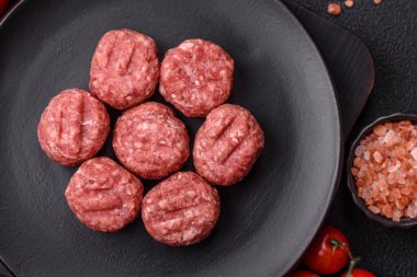 Çiğ et köftesi, domuz eti ya da tuzlu tavuk, baharat ve ottan oluşan koyu beton bir arka planda.