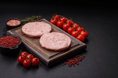 Raw chicken burger cutlet with salt, spices and herbs on dark concrete background clipart