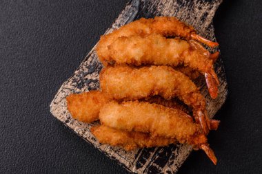 Sıcak gevrek karides, tuzlu ve baharatlı ve beyaz soslu, koyu beton arka planda.